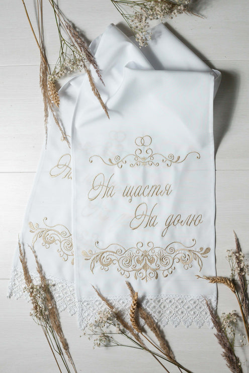 A white wedding rushnyk with gold-thread embroidery, displaying the phrase 'На щастя, На долю'.
