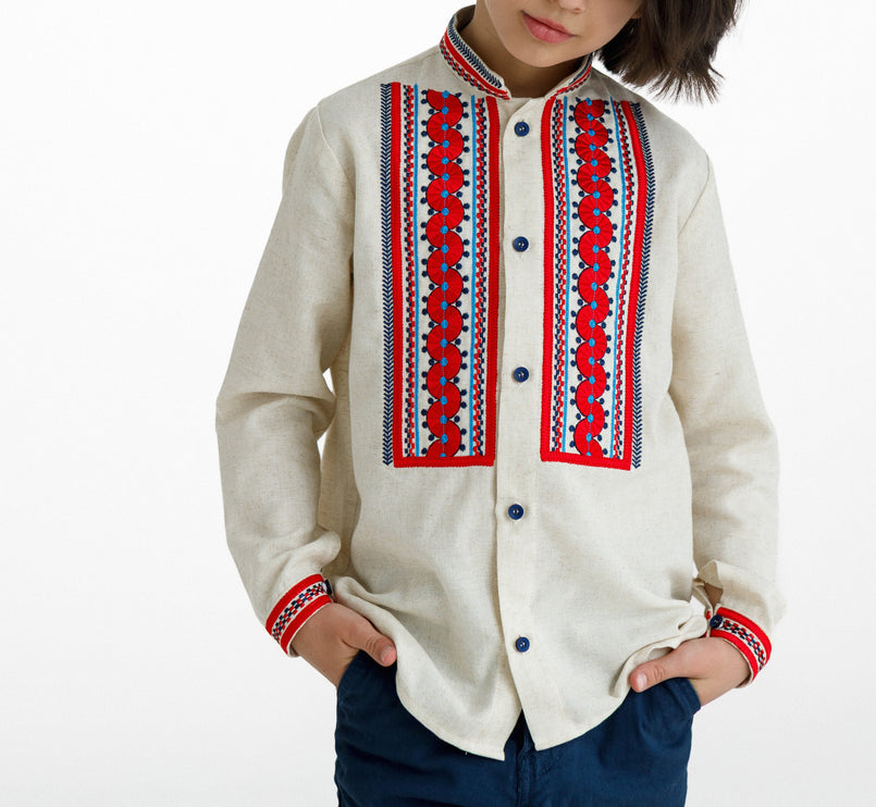 Front view of a boy’s natural linen embroidered shirt with red panels and cuffs, worn with navy trousers