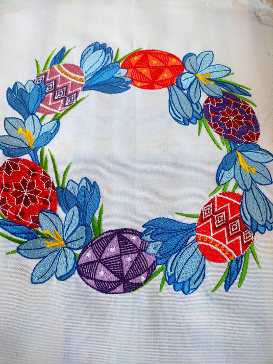 Embroidered wreath of blue crocuses and Easter pysanky on a white Ukrainian Easter rushnyk