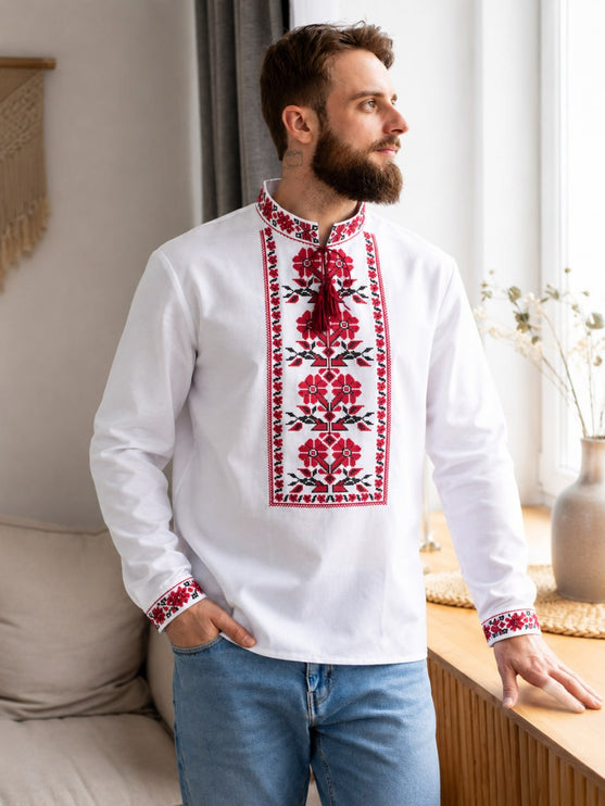 Bearded man in a white embroidered vyshyvanka shirt with red floral panel and jeans by a window