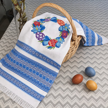 Ukrainian Easter rushnyk with blue crocus and pysanka wreath embroidery and blue woven borders over a basket