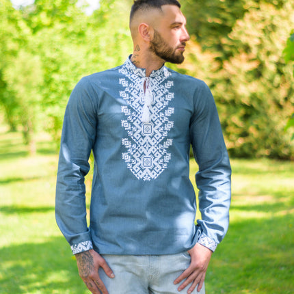 A man wearing a Ukrainian men's shirt with denim color and white embroidery.