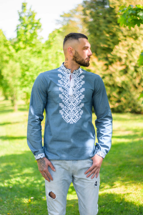 A man wearing a Ukrainian men's shirt with denim color and white embroidery.