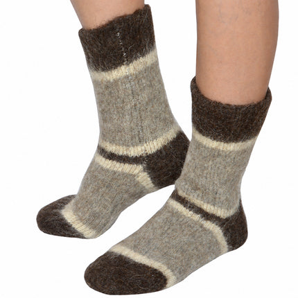 Feet wearing fuzzy gray-beige dog wool winter socks with brown cuffs and cream stripes