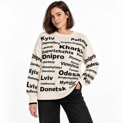 Woman wearing a cream oversized knit sweater with black Ukrainian city names and black jeans