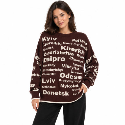 Woman wearing a chocolate brown oversized knit sweater with cream Ukrainian city names and black jeans