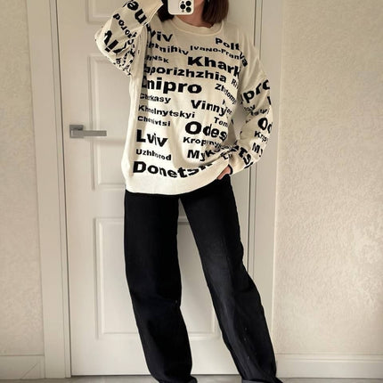 Full-length view of a cream Ukrainian cities knit sweater styled with black jeans and white sneakers