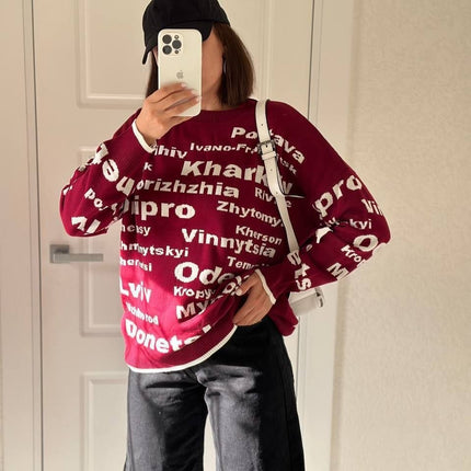 Mirror selfie of a woman in a burgundy Ukrainian cities knit sweater with a black cap