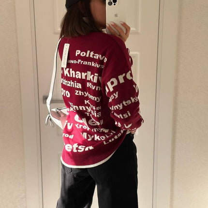 Side view of a burgundy oversized Ukrainian cities sweater with white lettering, worn with a black cap