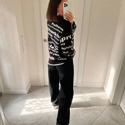 Woman in a black Ukrainian cities knit sweater and black trousers standing in a bright hallway