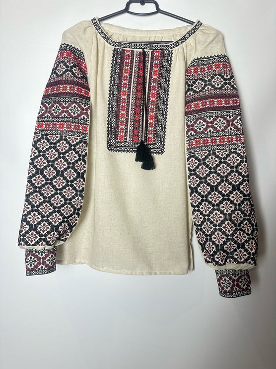 Flat lay of a women’s cream linen vyshyvanka blouse with red and black embroidered sleeves and neckline