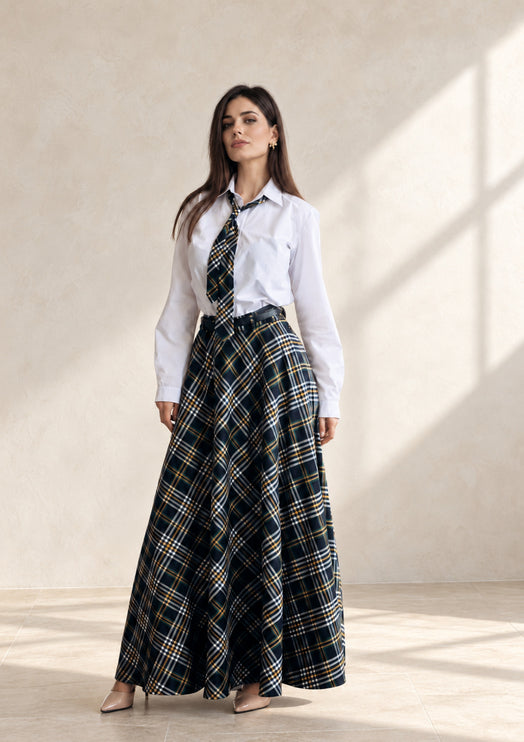 Woman wearing a plaid flared maxi skirt with matching necktie and white shirt in a sunlit room