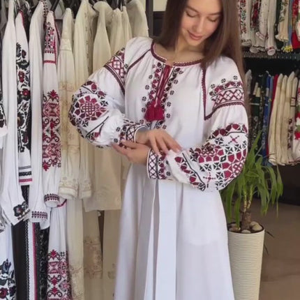Video of a woman wearing a white Ukrainian embroidered maxi dress with red ornament in a boutique