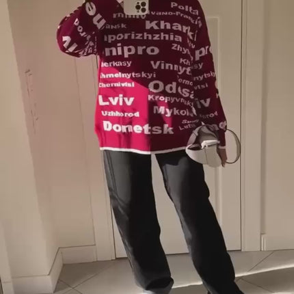Video of a woman showing a burgundy Ukrainian cities oversized knit sweater with white lettering