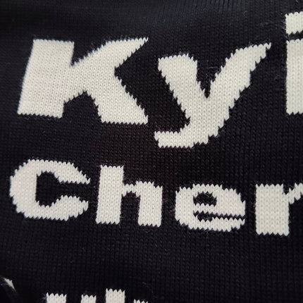 Detail of white Kyiv and Cherkasy lettering knitted into a black oversized Ukrainian cities sweater
